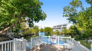 A wooden deck with white railings and benches overlooking a calm body of water, with a sign indicating no diving. - Tropical condo with 2 pools, private beach area, swimming lagoon, tennis & AC (Key Largo)
