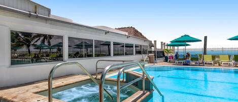 A swimming pool with a hot tub, lounge chairs, and umbrellas.