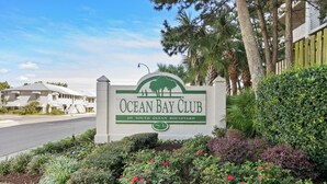Ocean Bay Club -kyltti, joka sijaitsee osoitteessa 201 South Ocean Boulevard. Sen ympärillä on vehreää kasvillisuutta ja taivaalla ei ole pilviä.