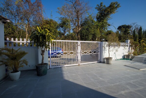 A gated entrance with a white picket fence, potted plants, and a blue car parked inside. - Alaya Stays Baramasa 3 BHK Hill Retreat (Dehradun)