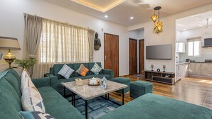 A modern living room with a sectional sofa, a coffee table, and a dining area with a kitchen in the background. - Alaya Stays Baramasa 3 BHK Hill Retreat (Dehradun)