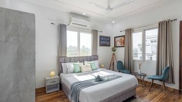 A modern bedroom with a large bed, a ceiling fan, an air conditioning unit, a tripod lamp, and a view of the city through the window.