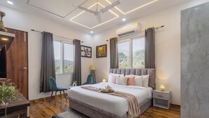 A modern bedroom with a large bed, a ceiling fan, an air conditioning unit, a bedside table with a lamp, and a view of the outdoors. - Alaya Stays Baramasa 3 BHK Hill Retreat (Dehradun)
