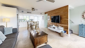 A modern living room with a sofa, coffee table, and TV. There is a kitchen in the background with white cabinets and a dining area. - Beach townhouse with shared pool, tennis & marina - AC, WiFi & snowbird-friendly (Key Largo)