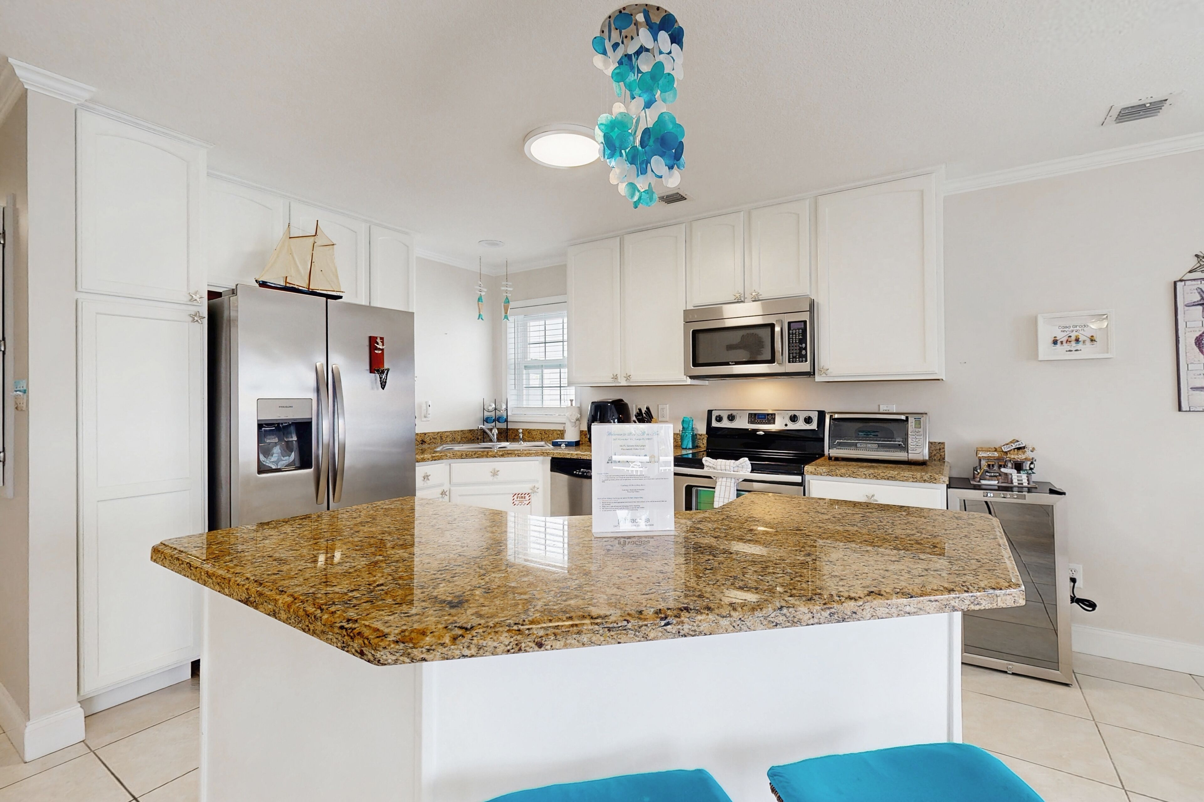 A modern kitchen with white cabinets, a granite countertop, stainless steel appliances, and a decorative ceiling light.