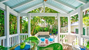 A covered outdoor area with a glass table and chairs, surrounded by lush greenery and a pool. - Charming dog-friendly home with guest cottage & private pool - great location (Key West)