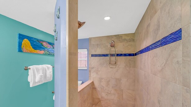 A bathroom with teal walls, a shower with beige tiles, and a blue mosaic border. - Charming dog-friendly home with guest cottage & private pool - great location (Key West)