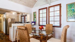 A dining area with wicker chairs and a glass table, a kitchen with white cabinets, and a large window with blinds. - Spacious Key West Conch Cottage with WiFi & Private Hot Tub - Dogs OK (Key West)