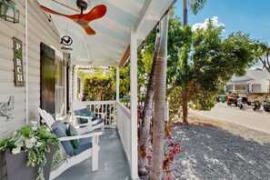 Une véranda avec des balustrades blanches, un ventilateur de plafond et des sièges d’extérieur.