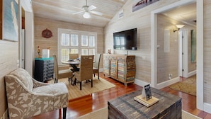 A spacious living room with a ceiling fan, a flat-screen TV, a dining area with wicker chairs, and a wooden cabinet with drawers. - Pool, Pet-friendly, Bicycles and 5 min walk to Beach (Key West)
