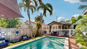A swimming pool with a wooden deck, lounge chairs, and a fence with palm trees. - Pool, Pet-friendly, Bicycles and 5 min walk to Beach (Key West)