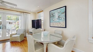 A dining area with a glass table, wicker chairs, a television, and a painting on the wall. - Ground-level getaway with free WiFi, private deck, & shared outdoor pool (Key West)