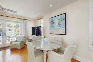 A dining area with a glass table, wicker chairs, a television, and a painting on the wall. - Ground-level getaway with free WiFi, private deck, & shared outdoor pool (Key West)