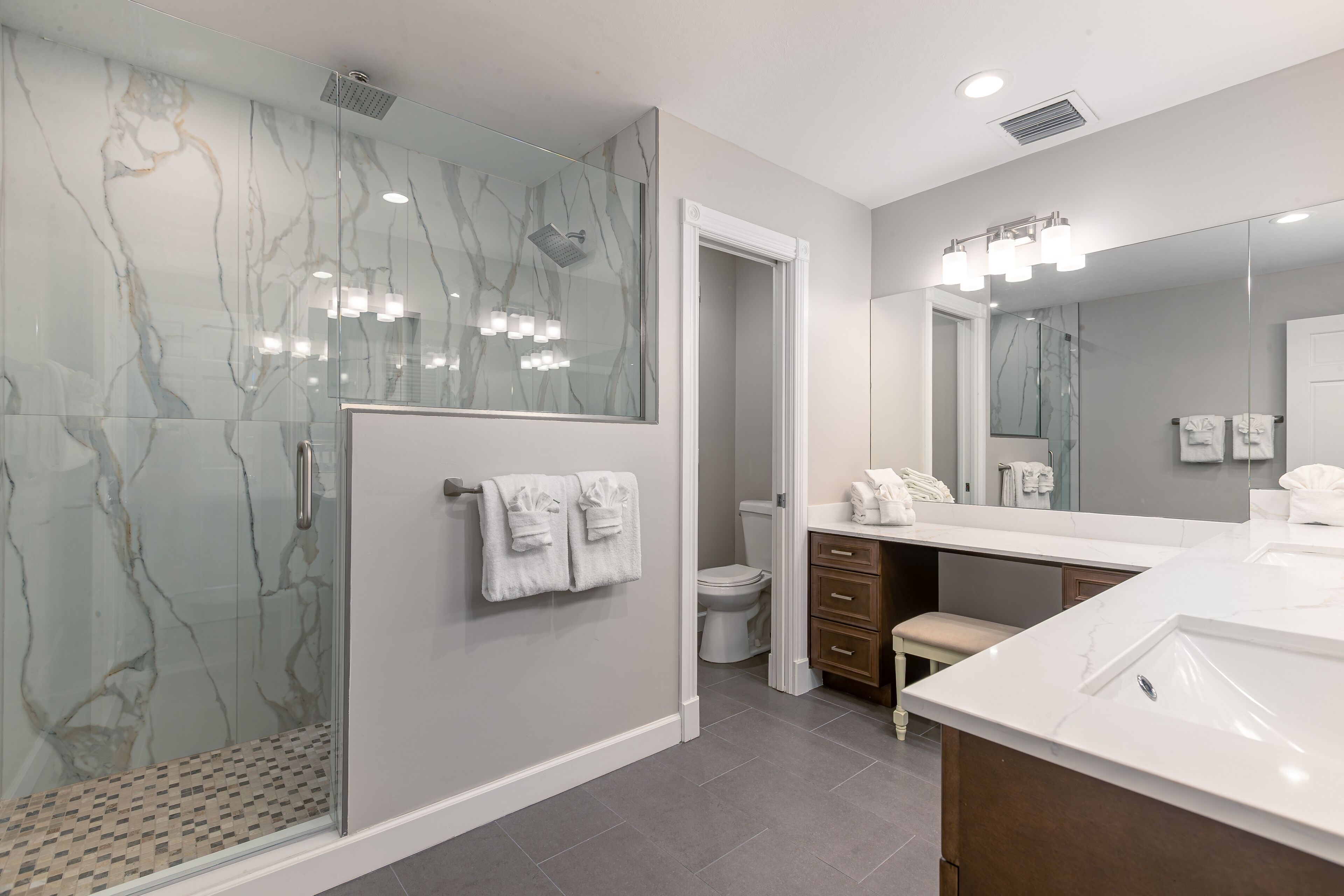 A modern bathroom with a glass-enclosed shower, a large mirror, and a vanity with a sink.