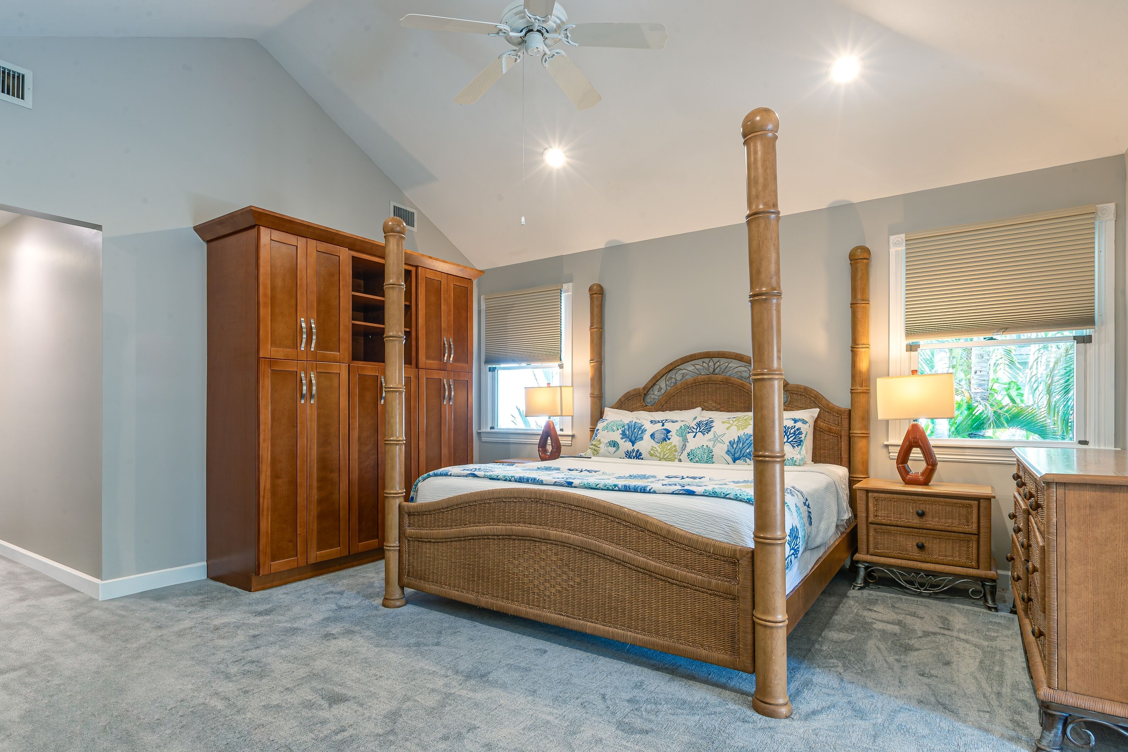 A bedroom with a four-poster bed, wooden wardrobe, and a ceiling fan.