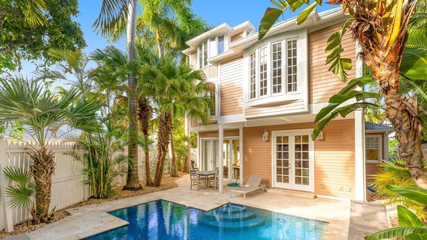 A two-story house with a swimming pool, surrounded by palm trees and a white fence. - The Southernmost Comfort House — Private Pool + Waterfall | 5BR Truman Annex Estate | 28-Day Stay (Key West)