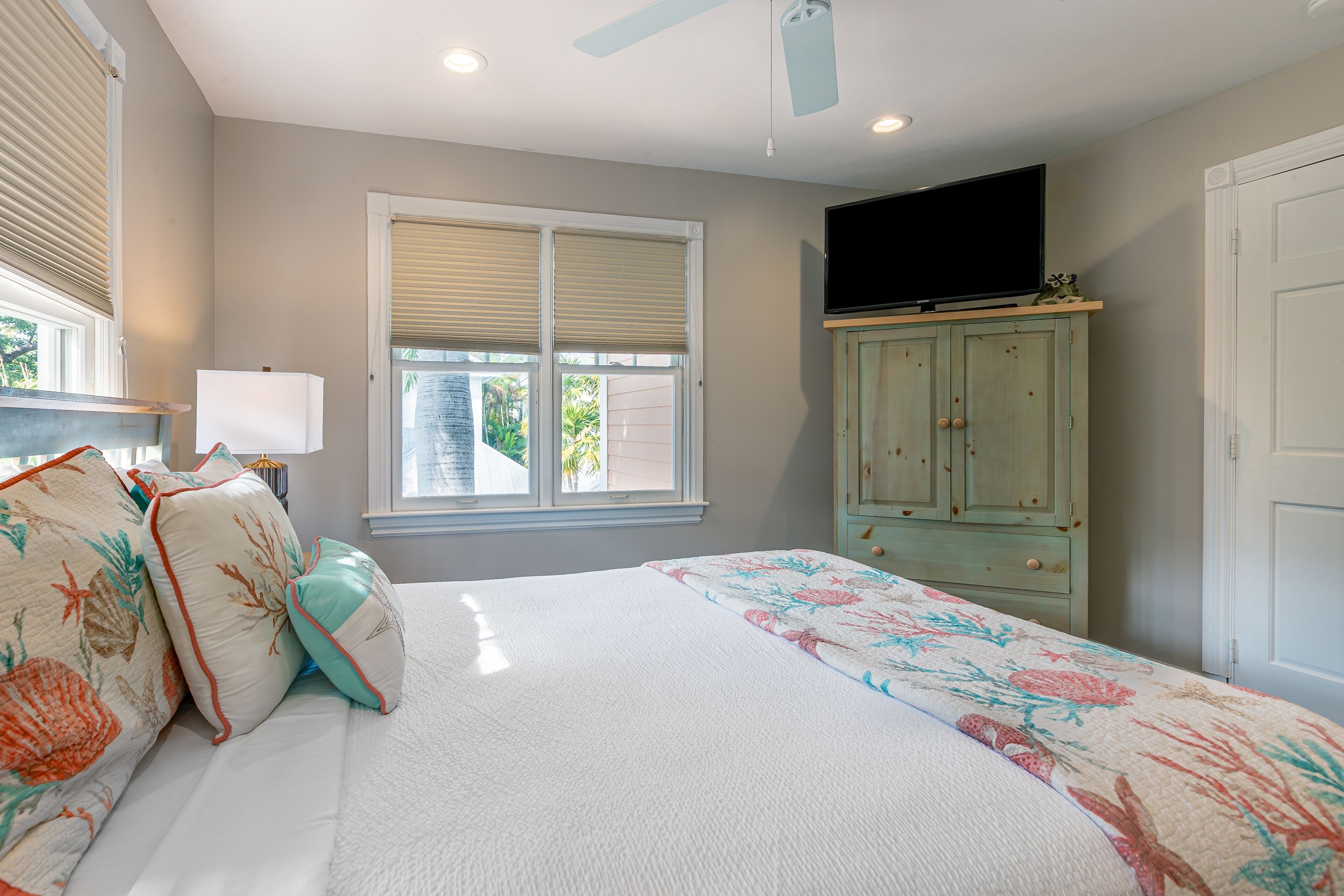 A bedroom with a bed, a television on a cabinet, and a window with blinds.