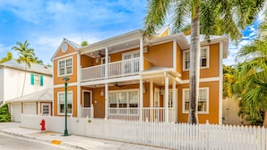 A two-story house with a white picket fence, a balcony, and a red fire hydrant on the sidewalk. - The Southernmost Comfort House — Private Pool + Waterfall | 5BR Truman Annex Estate | 28-Day Stay (Key West)