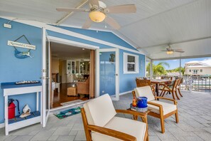 A covered outdoor area with wooden chairs and a table, a blue wall with a sign reading "Mermaid Crossing," and a view of a building in the background. - Dog-friendly home on a wide canal w/ WiFi & amazing water views (Tavernier)