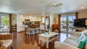 Amplia sala de estar con cocina, comedor y balcón con televisor.
