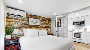 A modern bedroom with a large bed, a wooden accent wall, and a kitchenette with a microwave and oven. - Charming, updated home near Duval St. with enclosed patio & walkable location (Key West)