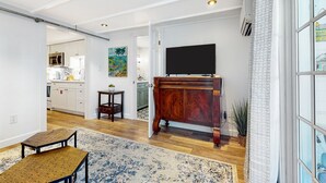 An open-plan living area with a wooden dining table, a TV mounted on a wooden cabinet, and a kitchen visible in the background. - Charming, updated home near Duval St. with enclosed patio & walkable location (Key West)