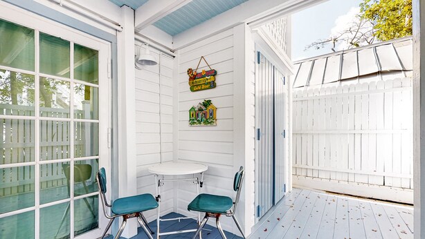 A covered porch with two green chairs, a small round table, and a white fence. - Charming, updated home near Duval St. with enclosed patio & walkable location (Key West)