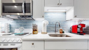 A modern kitchen with a stainless steel microwave, a gas stove, a sink, and a red coffee machine. - Charming, updated home near Duval St. with enclosed patio & walkable location (Key West)