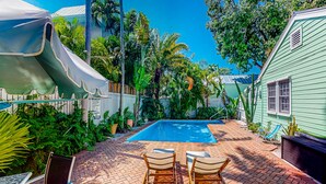 Ein Garten mit Schwimmbecken, zwei Liegestühlen und einer überdachten Terrasse.