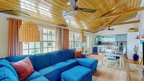 Ein geräumiges Wohnzimmer mit einem blauen Ecksofa, Holzboden und einem Essbereich mit einem weißen Tisch und Stühlen.