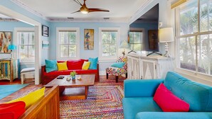 Een ruime woonkamer met een kleurrijk vloerkleed, een rode bank, een blauwe bank en een houten salontafel.