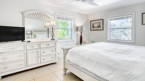 A bedroom with a bed, a TV, a dresser, two windows, and a ceiling fan. - Oceanfront Duplex with Beautiful Beach & Dock for Boat Access - Dogs OK (Long Key)
