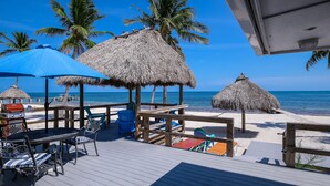 A wooden deck with a table and chairs, thatched umbrellas, and a view of the beach and ocean. - Oceanfront Duplex with Beautiful Beach & Dock for Boat Access - Dogs OK (Long Key)