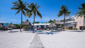 A beachside hotel with a wooden walkway leading to the building, surrounded by palm trees and thatched umbrellas. - Oceanfront Duplex with Beautiful Beach & Dock for Boat Access - Dogs OK (Long Key)