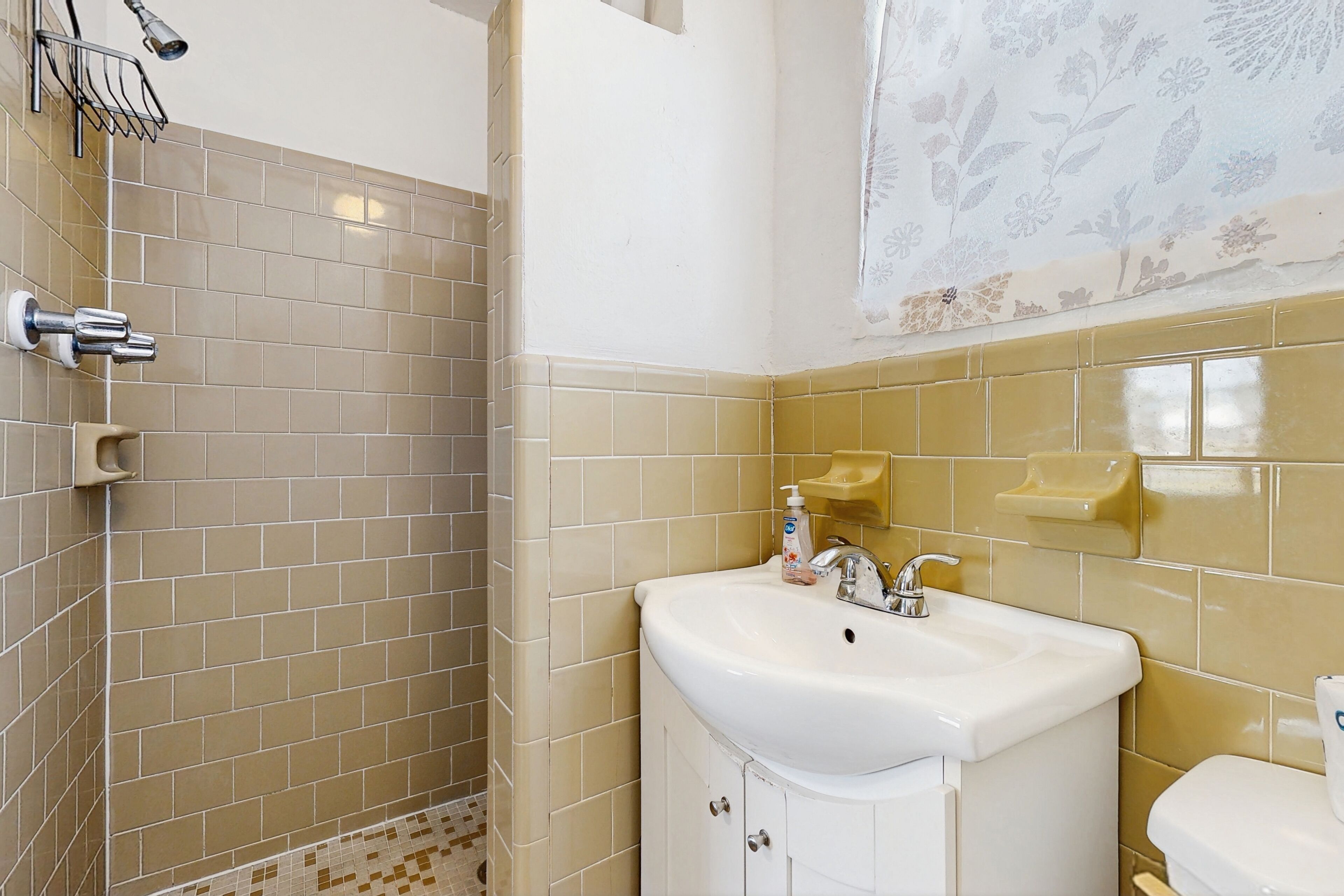 Uma casa de banho com azulejos bege, uma sanita branca, uma pia e uma área de duche.