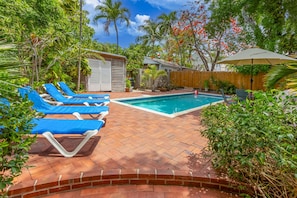 A backyard with a swimming pool, blue lounge chairs, and a wooden fence.
