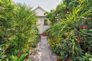 A pathway leading to a house surrounded by lush greenery and flowering plants.