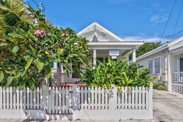 A historic inn with a white facade, a covered porch, and lush tropical foliage.
