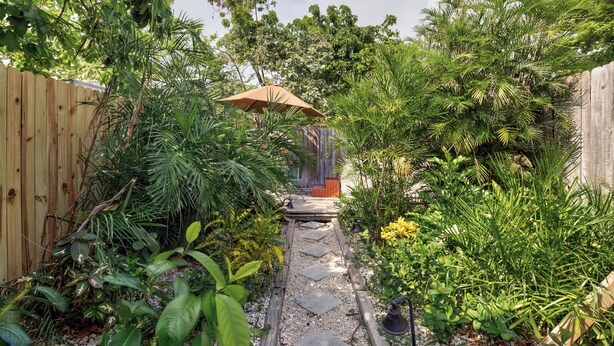 A garden pathway leading to a wooden deck with a bench, surrounded by lush greenery and a wooden fence.