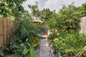 A garden pathway leading to a wooden deck with a bench, surrounded by lush greenery and a wooden fence.