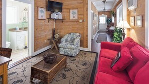 A living room with a red sofa, a patterned armchair, a wicker coffee table, and a television mounted on the wall.