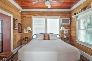 A bedroom with a large bed, wooden walls, a ceiling fan, and a window with blinds.