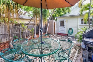 Une terrasse avec une table et des chaises en métal vert, un parasol suspendu et un barbecue.