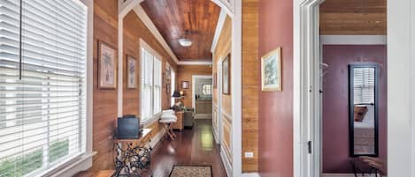 A hallway with wooden floors, white trim, and a view into a bedroom with a bed and a window.
