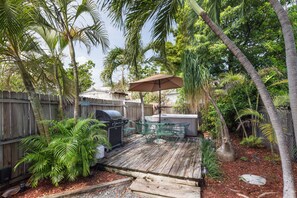 Une terrasse en bois avec un barbecue, du mobilier d’extérieur et un parasol.