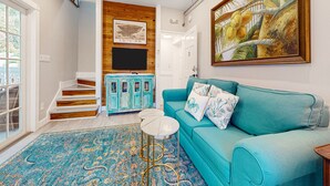 Una sala de estar con un sofá color turquesa, un tapete estampado, una escalera de peldaños de madera y un cuadro de cocos.