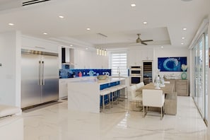 A modern kitchen with a central island, stainless steel appliances, and a blue backsplash. - Sprawling waterfront home with pool, outdoor kitchen, game table, grill, & W/D (Key Largo)