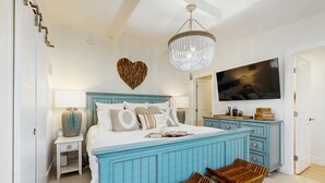 Een slaapkamer met een groot bed, een televisie, een kroonluchter en een hartvormige decoratie aan de muur.