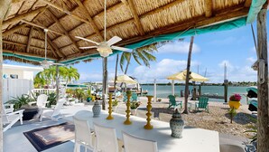 Een terras met witte stoelen en tafels, een rieten dak en parasols.