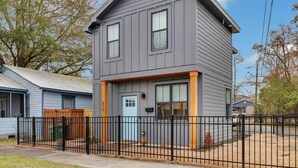 A two-story residential building with a gray exterior, a blue door, and a black metal fence.